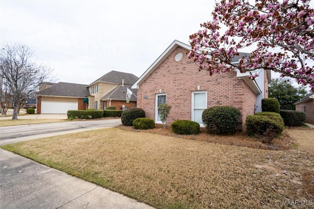 view of side of property featuring a yard, brick siding, and concrete driveway