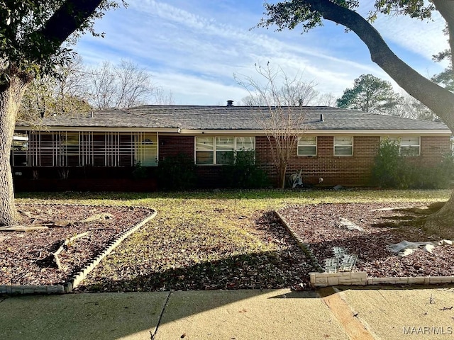 ranch-style home with a shingled roof, a front yard, and brick siding