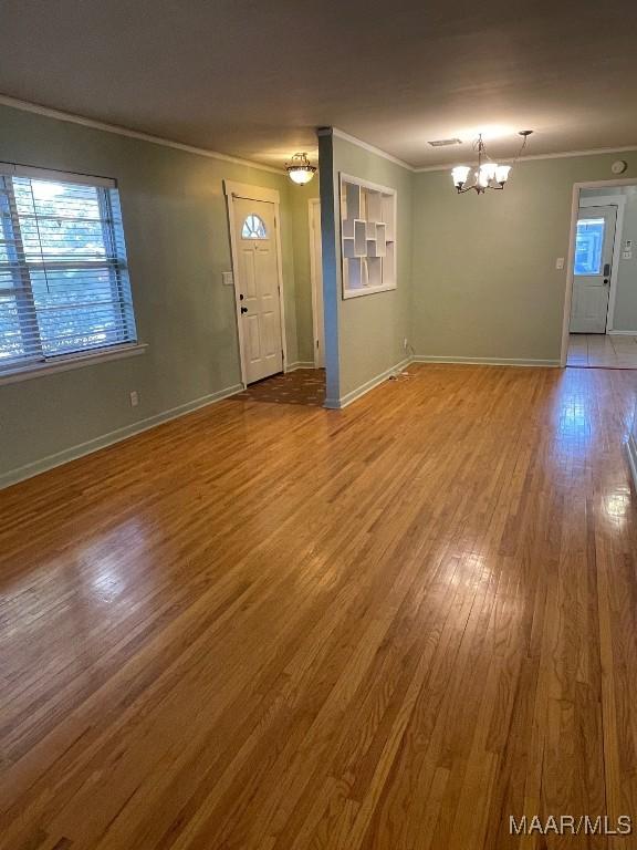 unfurnished living room featuring a notable chandelier, crown molding, visible vents, wood finished floors, and baseboards