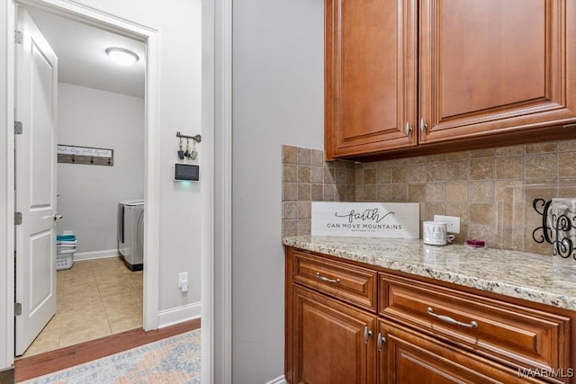 kitchen with brown cabinetry, light stone countertops, washer / dryer, light tile patterned flooring, and backsplash