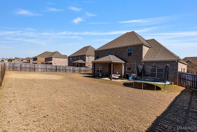 view of yard with a residential view, a trampoline, a fenced backyard, and a patio area