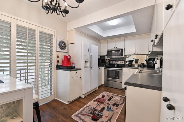 kitchen with dark countertops, a raised ceiling, appliances with stainless steel finishes, white cabinets, and a sink