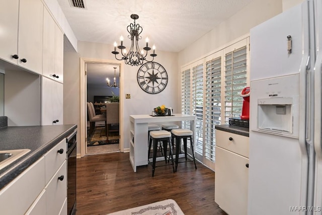 kitchen with dark countertops, decorative light fixtures, white fridge with ice dispenser, white cabinetry, and a notable chandelier