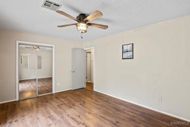 unfurnished bedroom with baseboards, visible vents, wood finished floors, a textured ceiling, and a closet