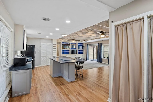 kitchen featuring visible vents, dark countertops, a breakfast bar area, open floor plan, and light wood-style floors