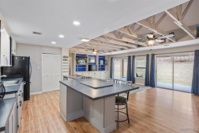 kitchen featuring white cabinets, dark countertops, ceiling fan, a kitchen island, and a kitchen bar