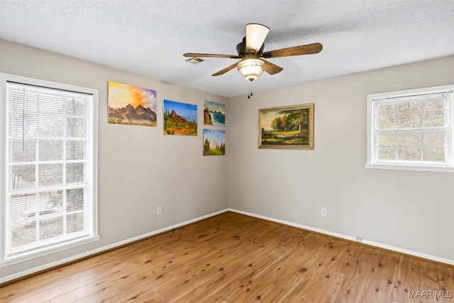 empty room featuring a ceiling fan, visible vents, a textured ceiling, and wood finished floors