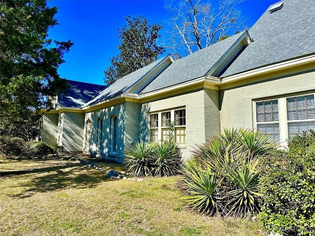 view of side of home with roof with shingles, a lawn, and brick siding