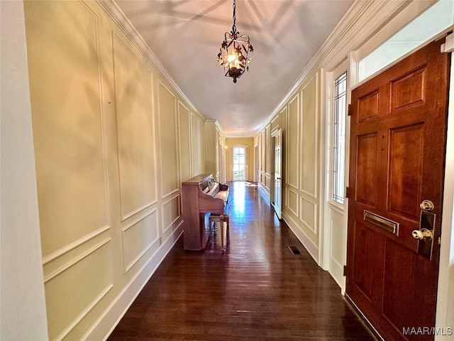 corridor featuring dark wood finished floors, a notable chandelier, visible vents, a decorative wall, and ornamental molding