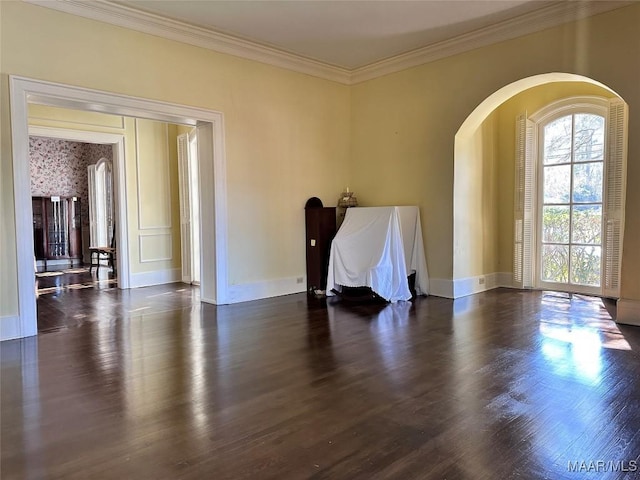 empty room with arched walkways, dark wood-style flooring, crown molding, and baseboards