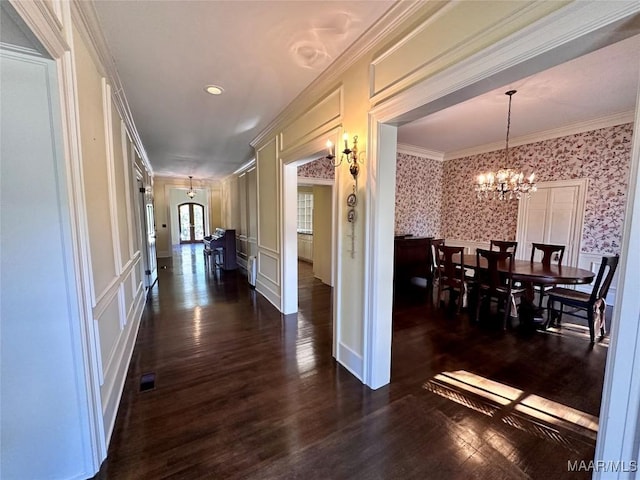 interior space featuring wallpapered walls, dark wood-style flooring, crown molding, a chandelier, and a decorative wall