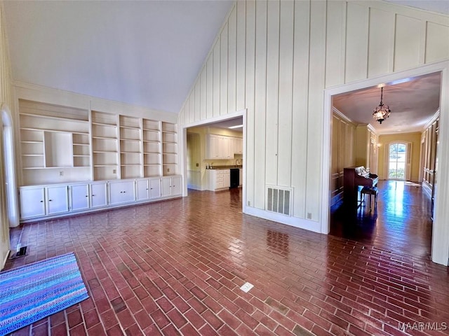 unfurnished living room featuring brick floor, visible vents, a notable chandelier, and high vaulted ceiling