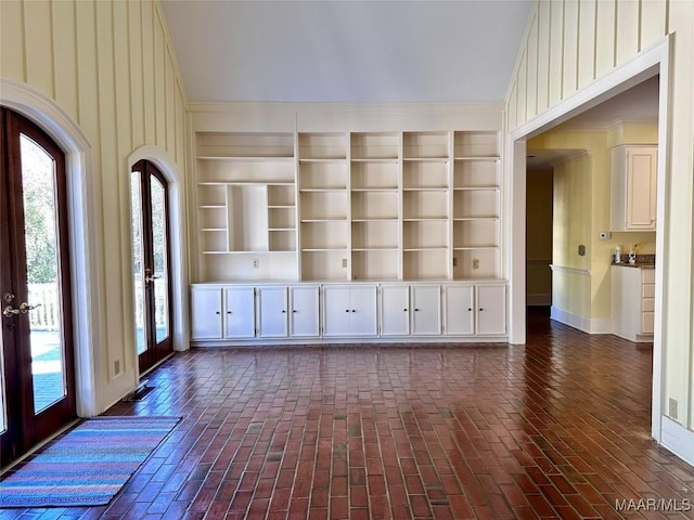 unfurnished room with visible vents, built in features, brick floor, vaulted ceiling, and french doors