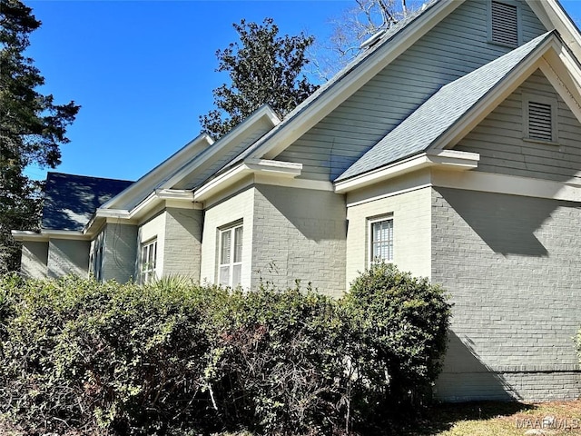 view of side of home with brick siding and roof with shingles