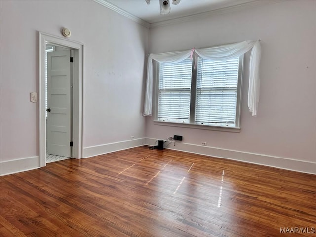 spare room with baseboards, wood finished floors, and crown molding