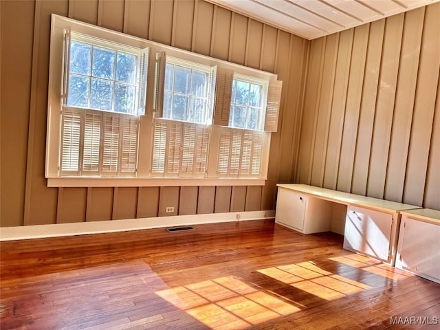 unfurnished room featuring visible vents, wood walls, light wood-style flooring, and built in study area