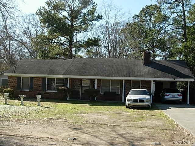 ranch-style home featuring brick siding, driveway, a carport, a front lawn, and a chimney