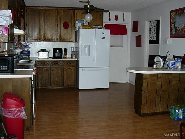 kitchen featuring black microwave, dark wood-style flooring, light countertops, decorative backsplash, and white fridge with ice dispenser