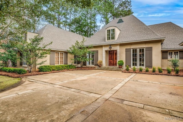 french country style house featuring roof with shingles and stucco siding