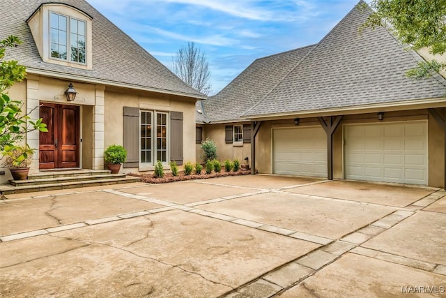 view of front facade featuring concrete driveway, a shingled roof, an attached garage, and stucco siding