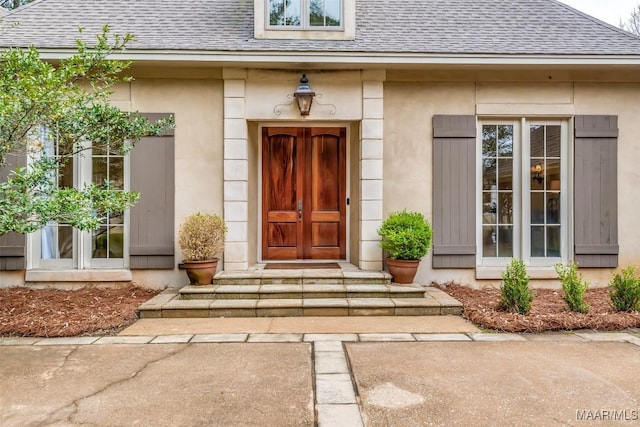 doorway to property with stucco siding and roof with shingles