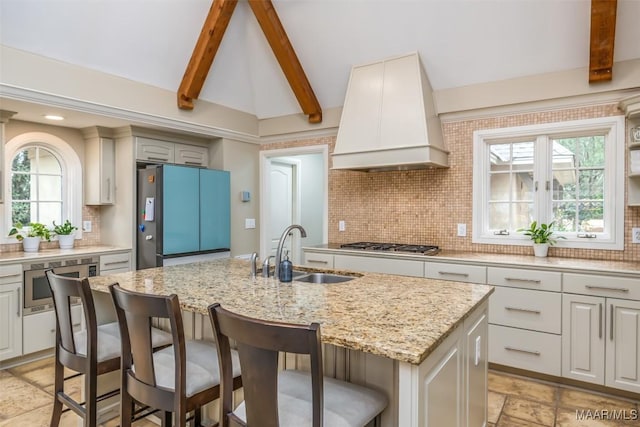 kitchen with light stone counters, a kitchen breakfast bar, a kitchen island with sink, custom exhaust hood, and a sink