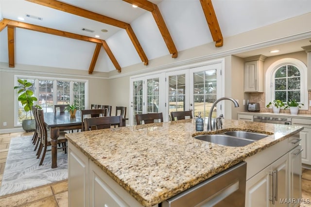 kitchen featuring lofted ceiling with beams, a kitchen island with sink, a sink, backsplash, and dishwasher