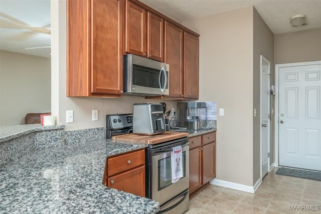 kitchen with appliances with stainless steel finishes, dark stone counters, brown cabinets, and baseboards
