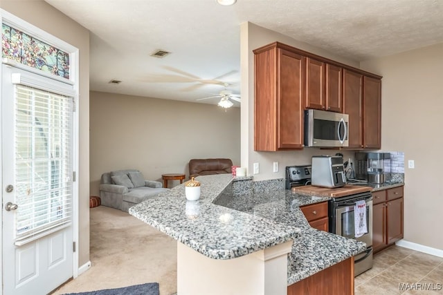 kitchen with light stone counters, brown cabinets, stainless steel appliances, open floor plan, and a peninsula