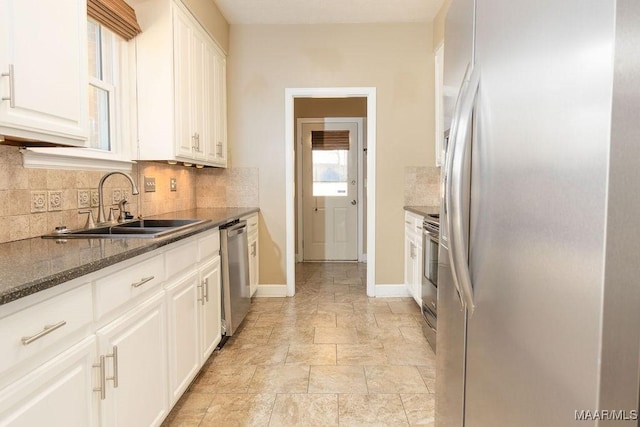 kitchen with appliances with stainless steel finishes, dark stone countertops, a sink, and white cabinetry