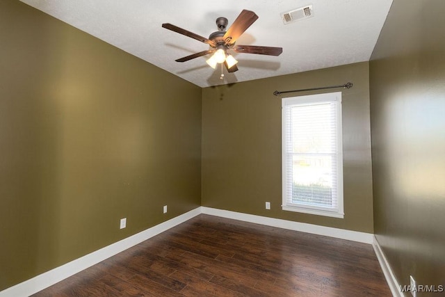 unfurnished room with dark wood-style floors, visible vents, baseboards, and a ceiling fan