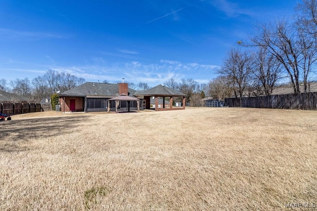 rear view of property with fence, a chimney, a gazebo, and a lawn