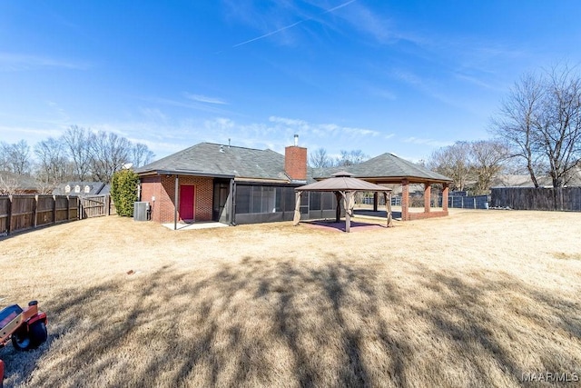 back of house featuring brick siding, a chimney, a gazebo, central AC unit, and a fenced backyard