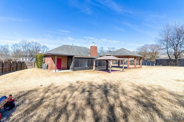 back of property featuring central AC unit, a fenced backyard, brick siding, a gazebo, and a chimney