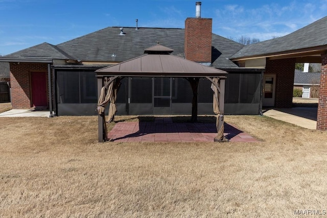 rear view of house featuring a sunroom, brick siding, a lawn, and a gazebo