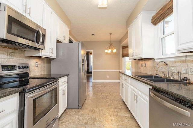 kitchen featuring stainless steel appliances, hanging light fixtures, white cabinets, a sink, and dark stone countertops