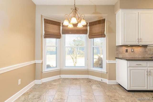 unfurnished dining area with plenty of natural light, baseboards, and an inviting chandelier