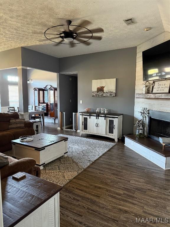 living room with a fireplace, dark wood finished floors, visible vents, a ceiling fan, and a textured ceiling