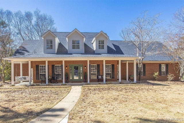 view of front of property featuring a shingled roof, covered porch, and brick siding