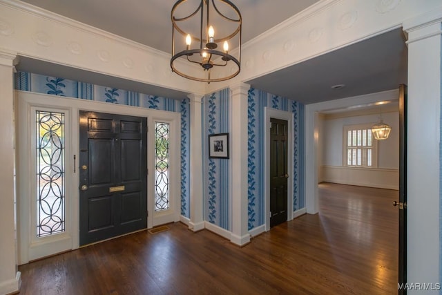 entrance foyer featuring dark wood-style floors, ornate columns, an inviting chandelier, baseboards, and wallpapered walls