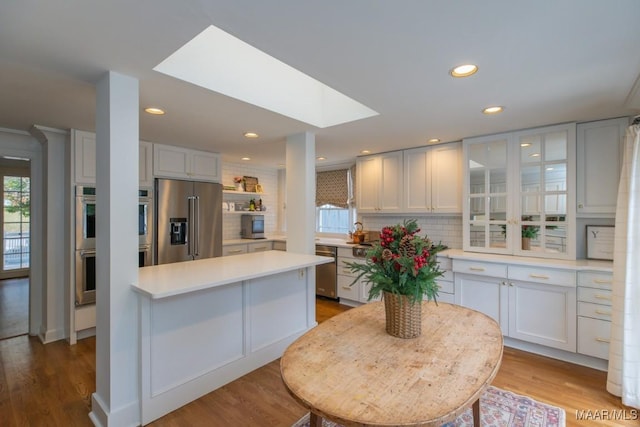 kitchen with white cabinetry, light countertops, appliances with stainless steel finishes, backsplash, and glass insert cabinets