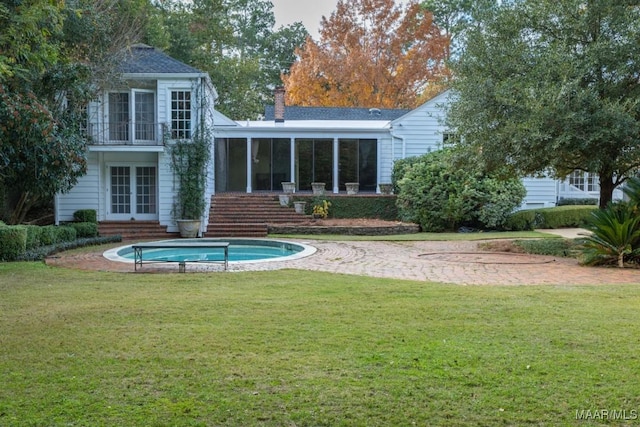 rear view of property featuring a sunroom, a chimney, stairway, and a lawn