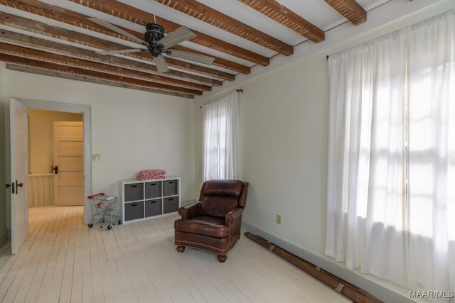 living area with beam ceiling, a healthy amount of sunlight, ceiling fan, and wood finished floors