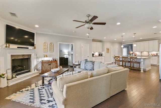 living area with dark wood-style floors, a tiled fireplace, visible vents, and crown molding