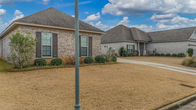 view of front facade featuring a front yard, brick siding, driveway, and roof with shingles