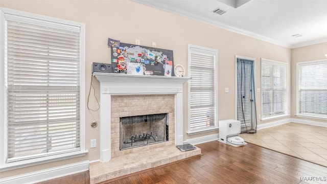 unfurnished living room with wood finished floors, visible vents, baseboards, ornamental molding, and a brick fireplace