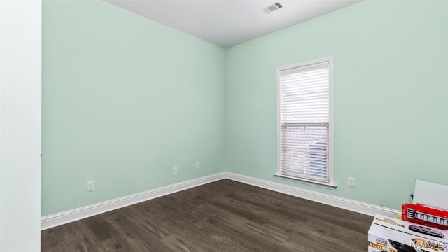 unfurnished room featuring dark wood-style floors, visible vents, and baseboards