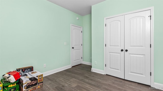 unfurnished bedroom with a closet, dark wood finished floors, and baseboards