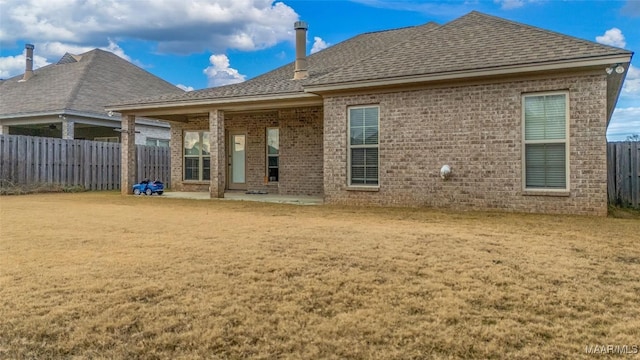 rear view of property with brick siding, a shingled roof, fence, a lawn, and a patio area