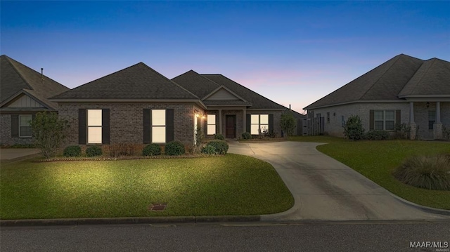 view of front facade featuring driveway, brick siding, and a lawn